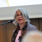 Eine Frau mit grauen schulterlangen Haaren und roter Brille steht an einem Rednerpult.