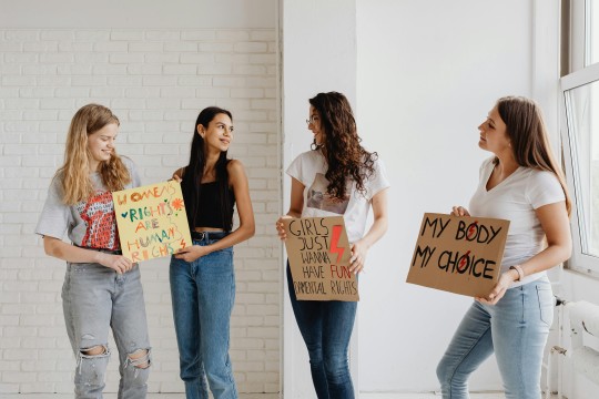 Man sieht eine Gruppe von Frauen, die unterschiedliche Schilder in die Kamera halten. Darauf kämpfen sie für mehr Frauenrechte. 