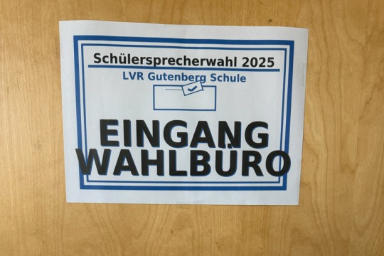 An einer Tür hängt ein Blatt. Es zeigt den Eingang zum Wahlbüro