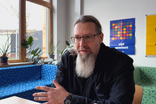 Ein Mann sitzend in einer Gesprächssituation. Er blickt an der Kamera vorbei.