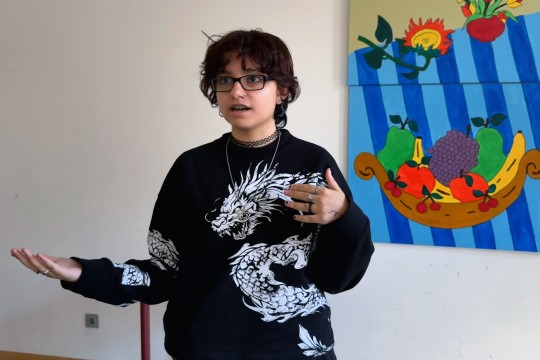 Eine stehende Schülerin redet und gestikuliert. Sie blickt an der Kamera vorbei.